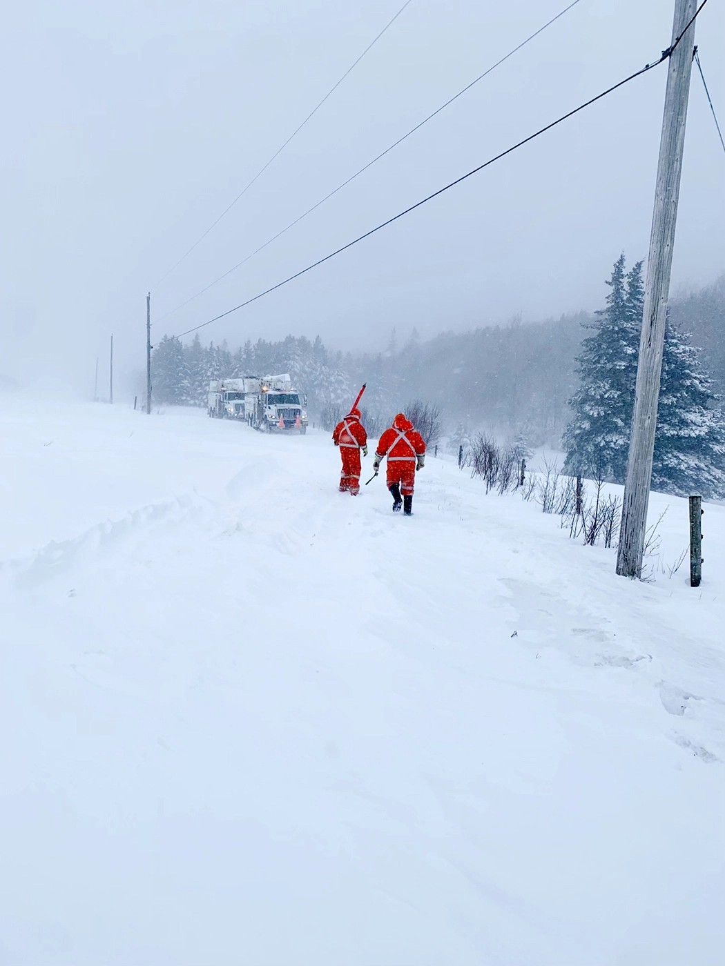 A place covered with deep snow with 2 workers wearing protective orange jackets walking