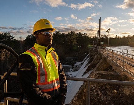 Nova Scotia employee in hard hat, goggles and safety vest standing near a dam