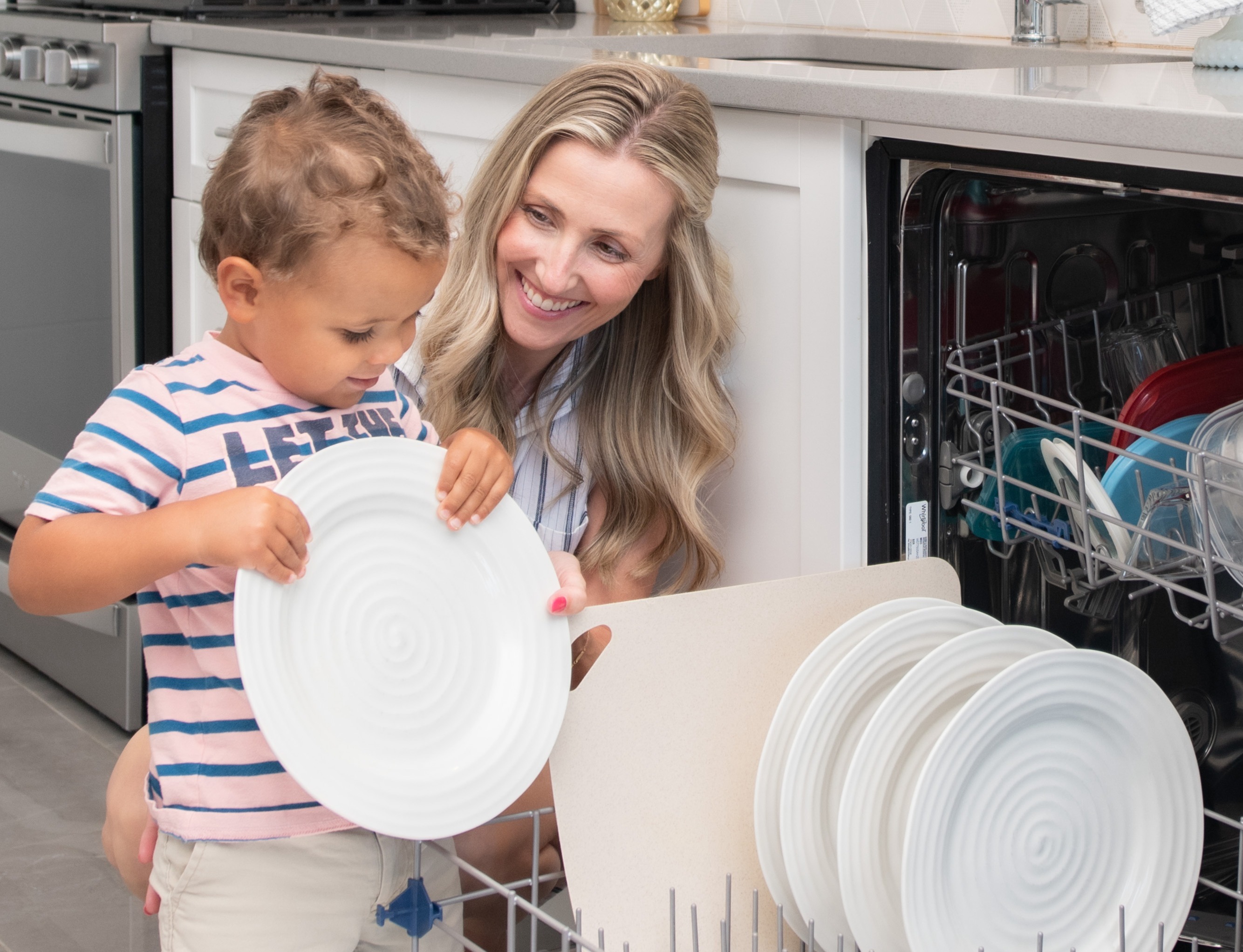 Mother with a child holding a plate by a dishwasher